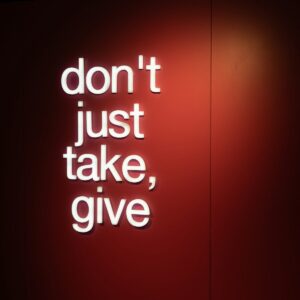 a red wall with a neon sign that says don't just take, give